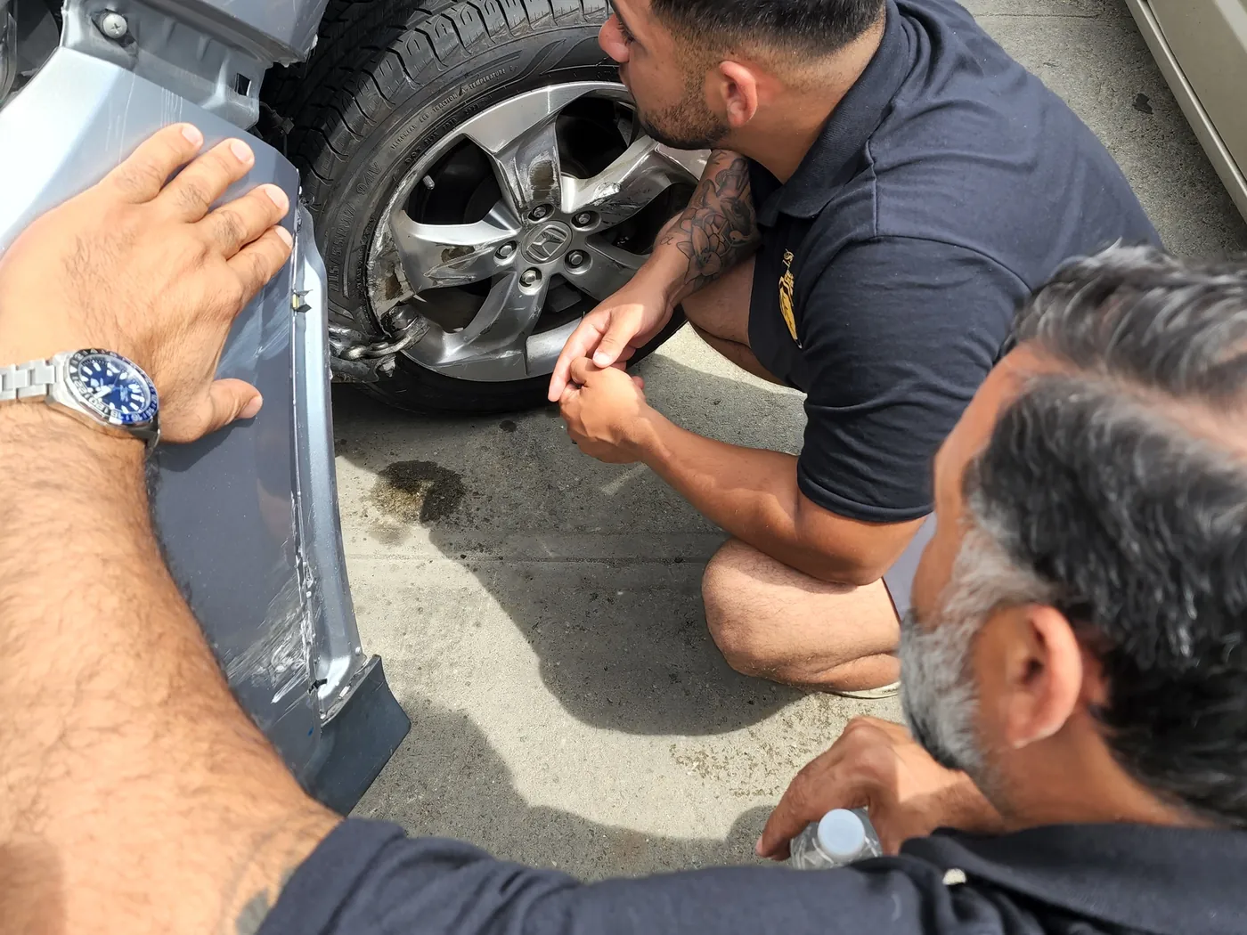 First Class Collision technicians inspecting collision damage on a wheel and fender
